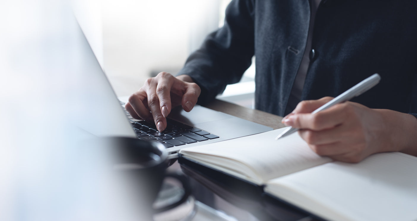 person using laptop and notebook to stay organised